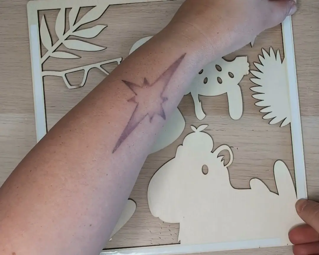 Arm liggend over een onbewerkte houten laag met capybara- en bladmotieven.