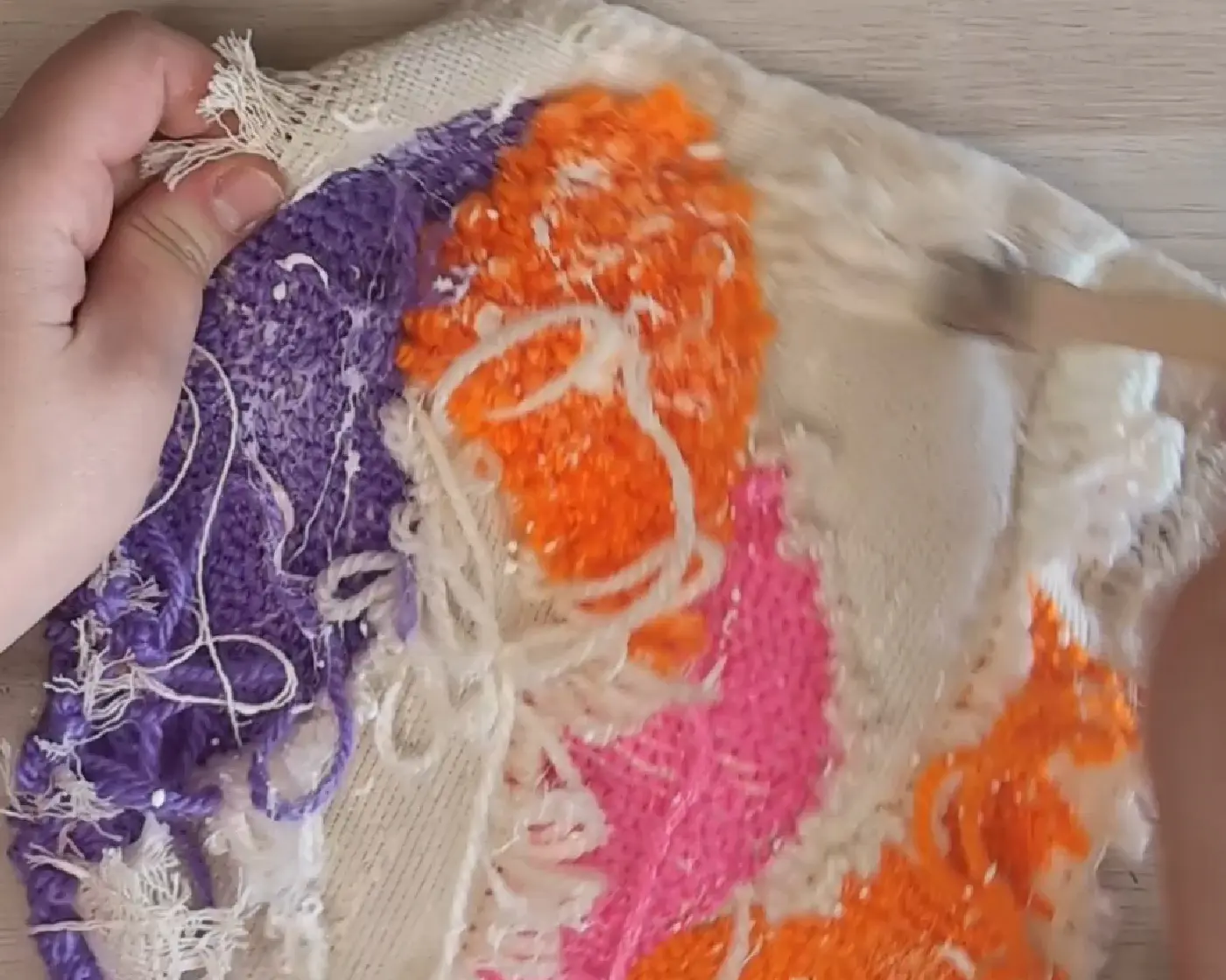 Achterkant van een punch needle werkstuk waarop de ruwe achterkant zichtbaar is met paarse, oranje en roze garenlussen
