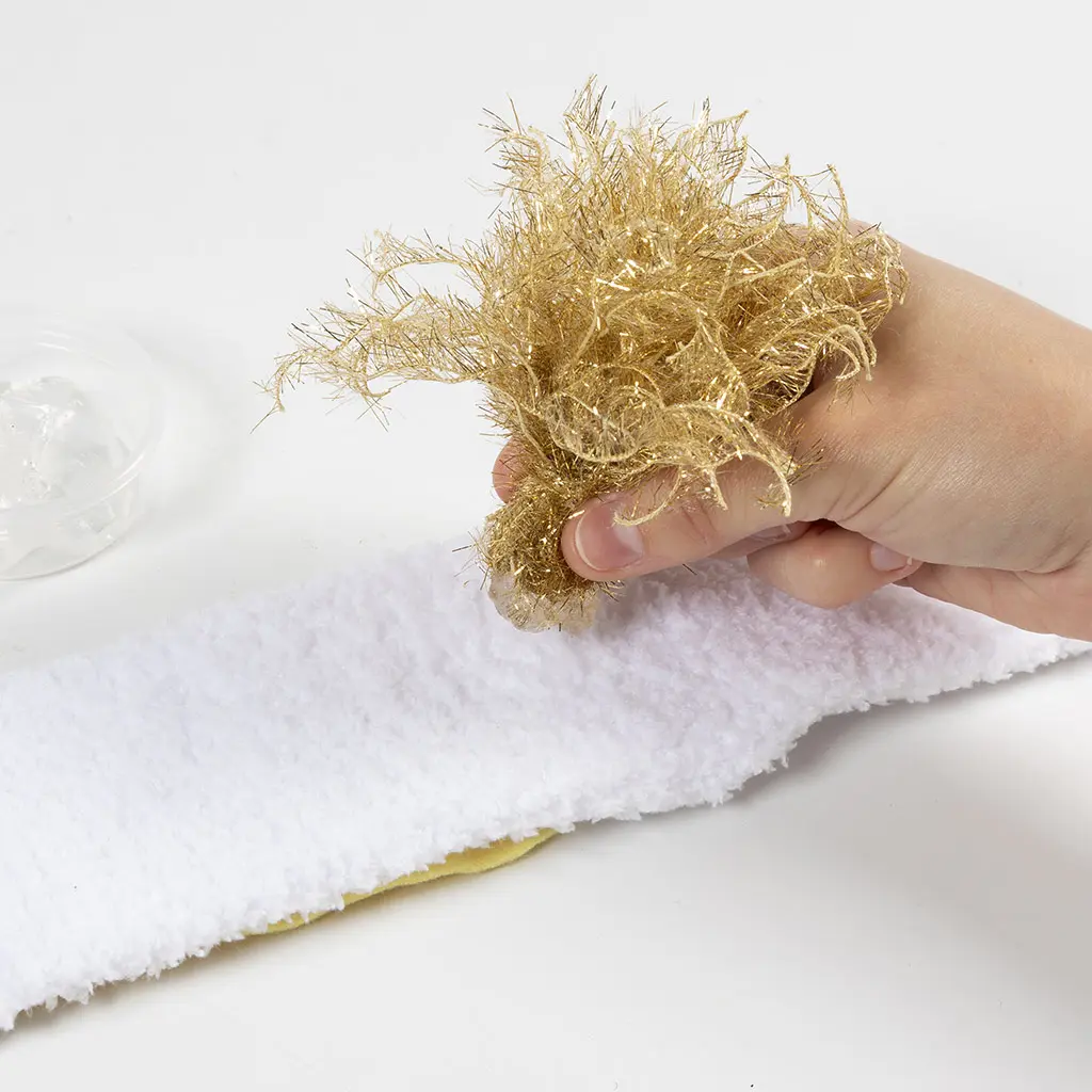 Het goudkleurige kwastje wordt op de neus van de pluizige witte sloef geplakt.