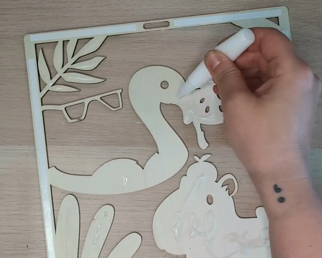 Hand brengt lijm aan op een onbewerkte houten laag met flamingo- en capybara-vormen om de lagen samen te voegen.