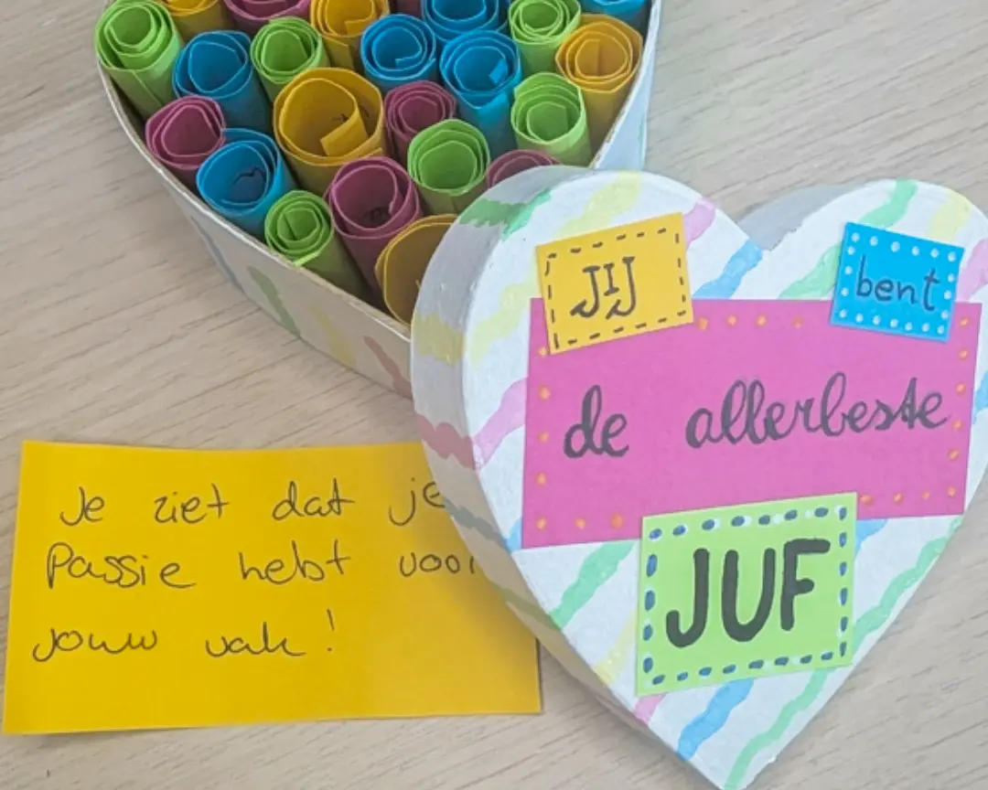 Het voltooide cadeau: een hartvormige doos vol opgerolde kaartjes in roze, blauw, geel en groen, met het deksel 
