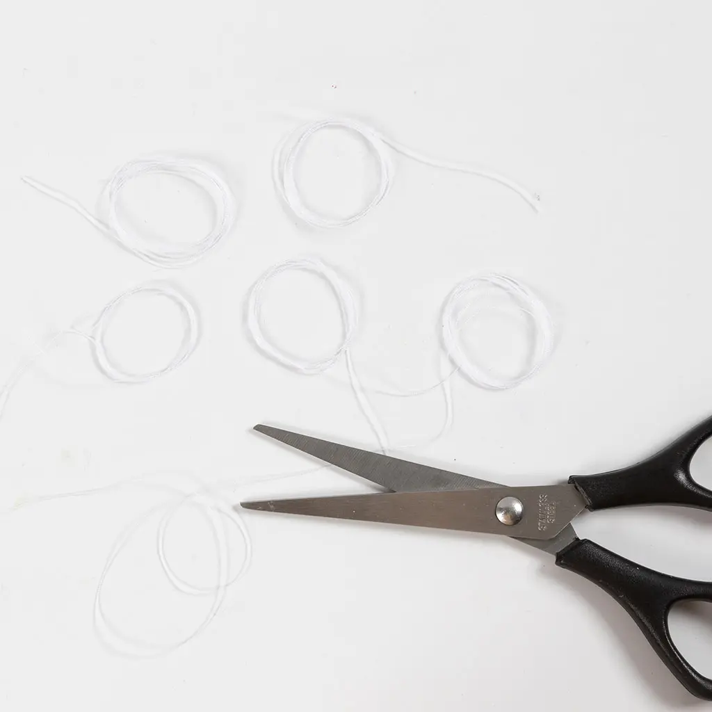 Vijf opgerolde stukken wit garen liggen op een witte achtergrond, met rechtsonder een schaar met zwarte handvaten die klaar ligt.