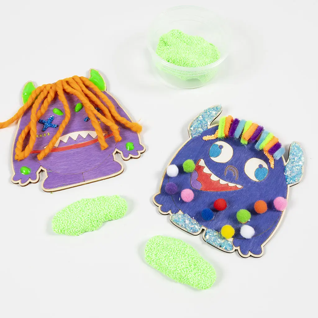 Bovenaanzicht van de twee versierde houten monsters. Er liggen drie klompjes felgroene Foam Clay op de witte tafel, waarvan één nog in een transparant plastic bakje zit.
