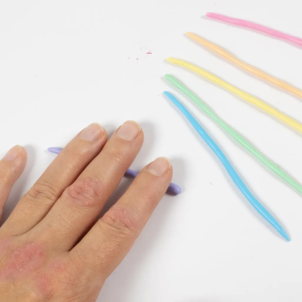 Een hand rolt dunne kleiworstjes in verschillende pastelkleuren op een witte ondergrond.