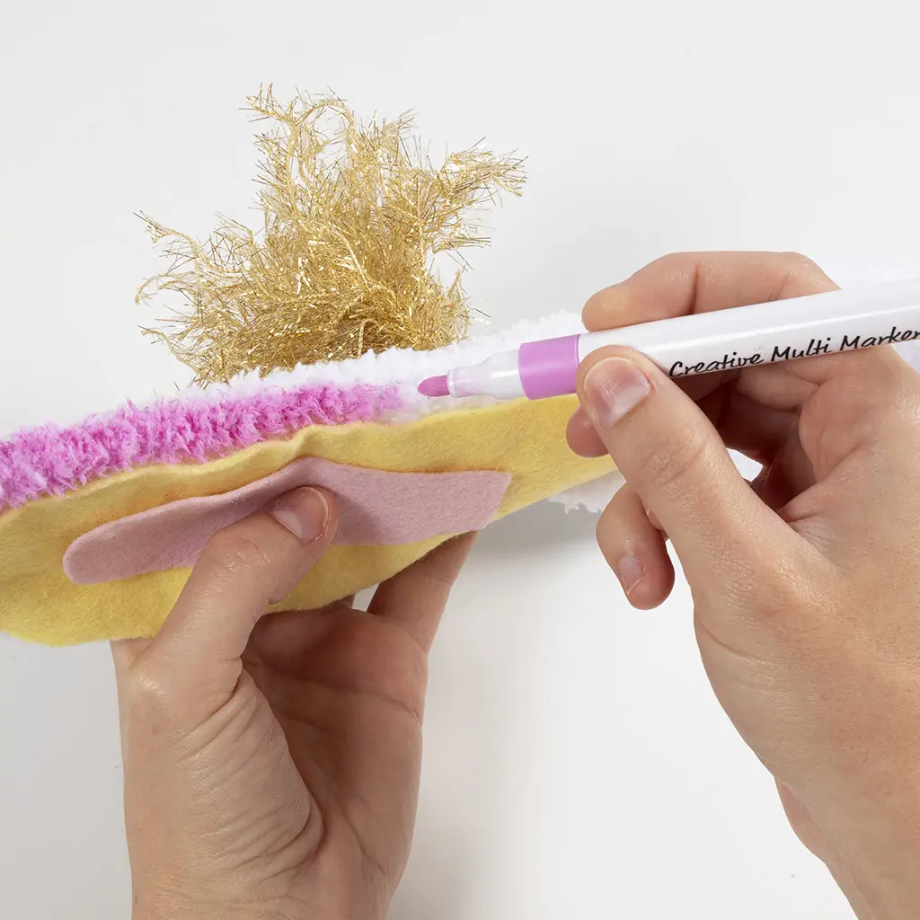 Met een roze stift wordt de harige rand van de witte pluizige stof roze gekleurd.