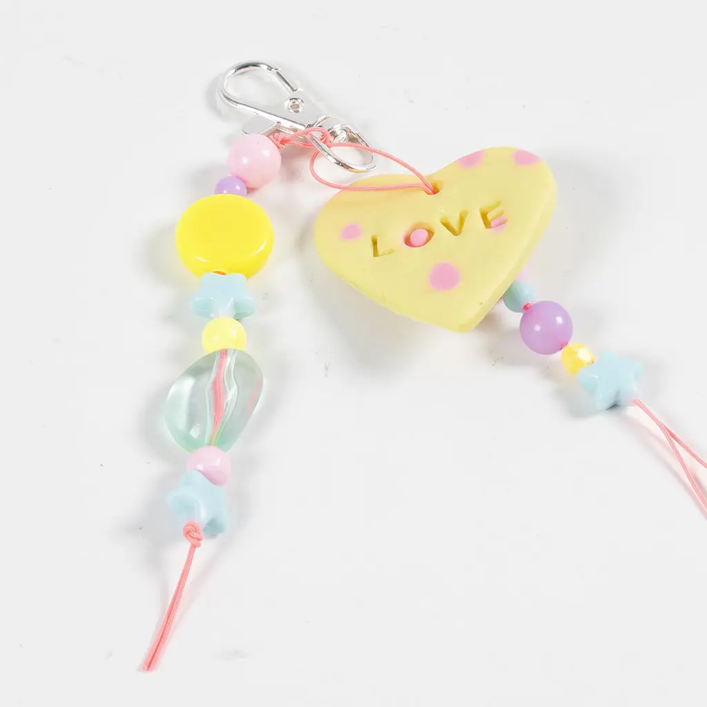 Het gele kleihartje met de tekst LOVE gemonteerd tussen de gekleurde kralen van de tasbedel.