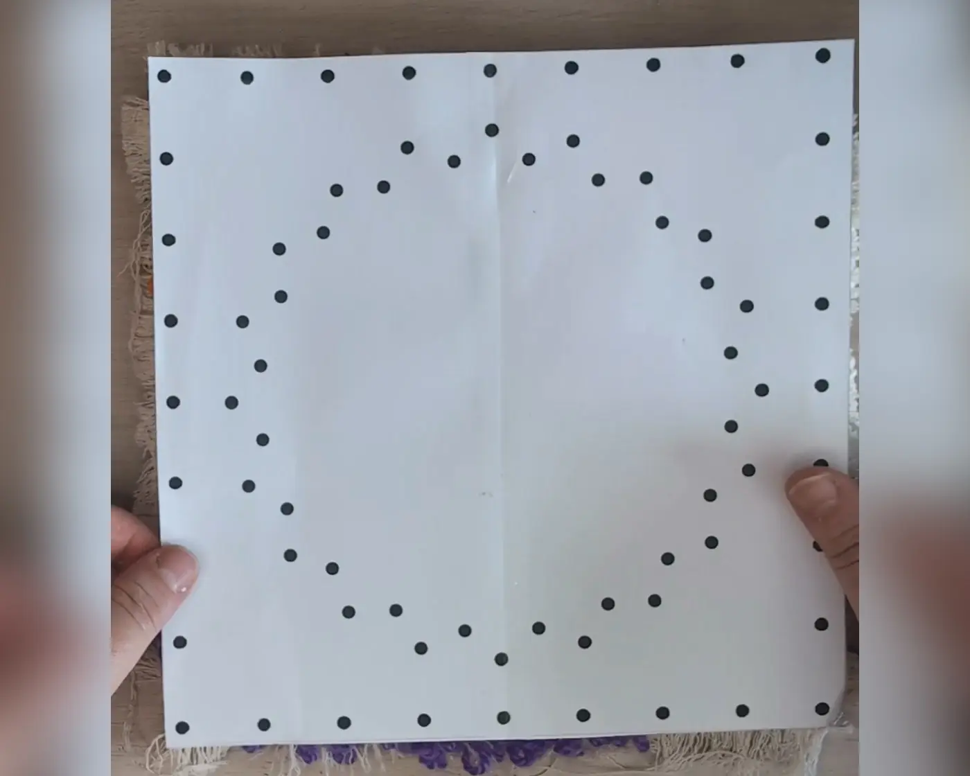 Twee handen houden een wit papier met zwarte stippen in een hartvorm als string art patroon
