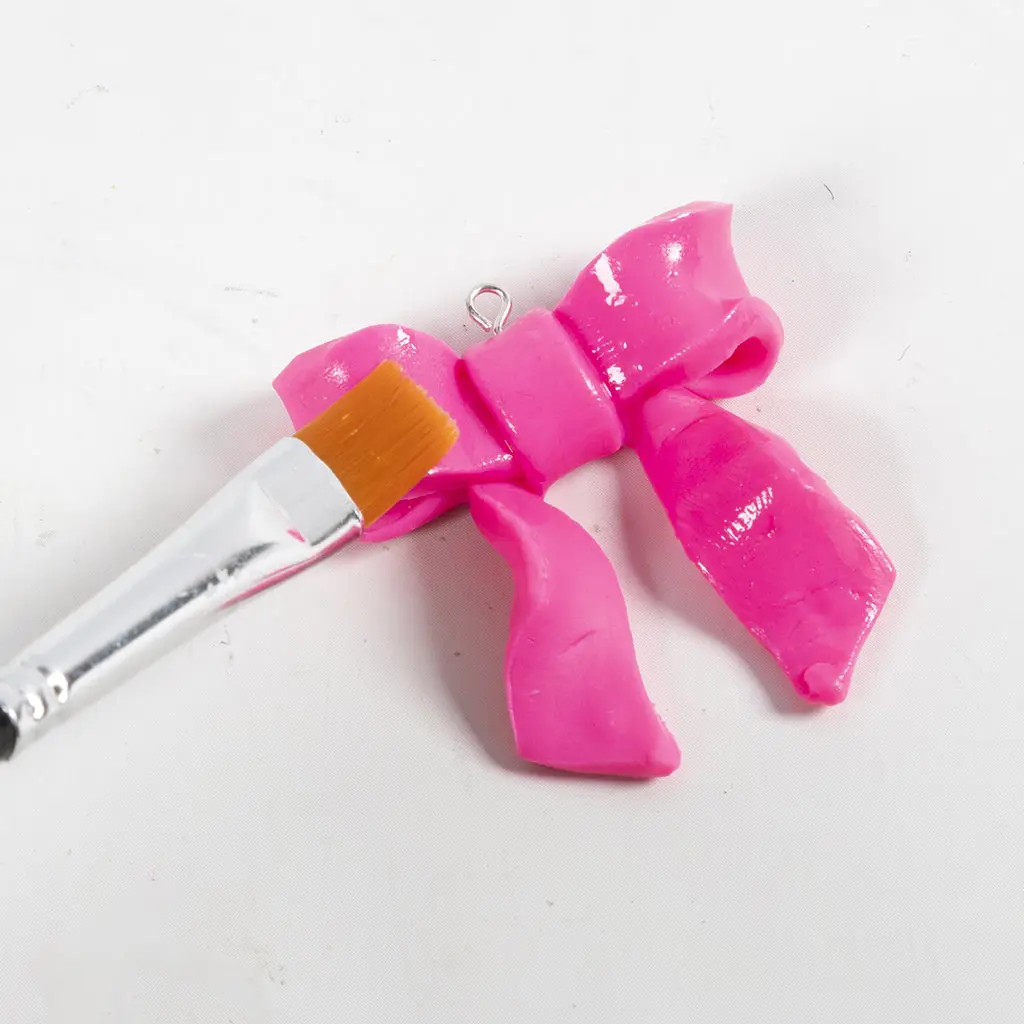 Een penseel brengt een glanzende, transparante laklaag aan op de roze polymeerkleistrik om deze een mooie glans te geven en te beschermen.