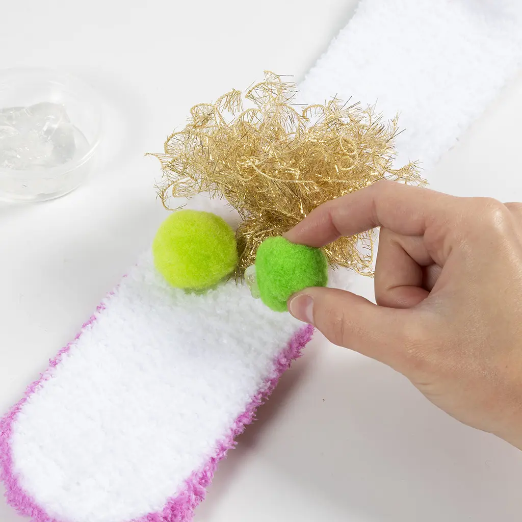 Twee felgroene pompoms worden als ogen achter het gouden kuifje op de pluizige sloef geplakt.