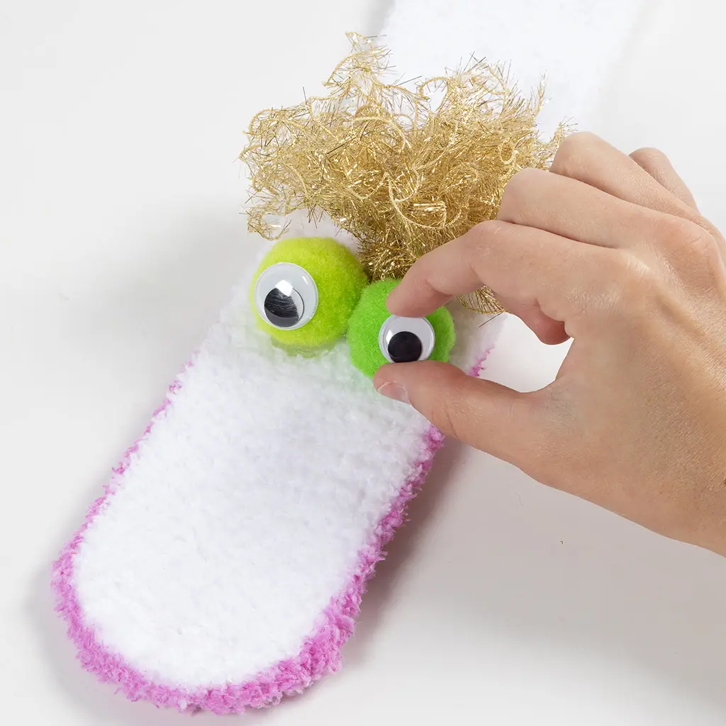 Wiebeloogjes worden op de groene pompoms geplakt om het gezichtje van de sloef af te maken.