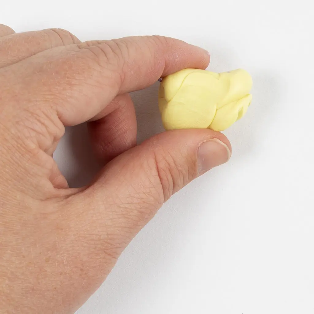 Een hand kneedt een lichtgeel stukje klei zacht ter voorbereiding op het uitrollen.