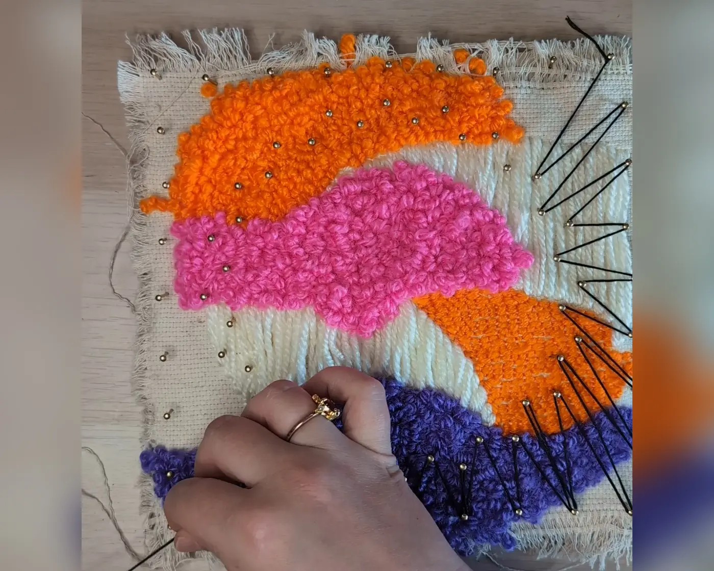 Punch needle werkstuk met oranje, roze en paars garen waarop aan de rechterkant al zwart string art garen is gespannen tussen de spijkers