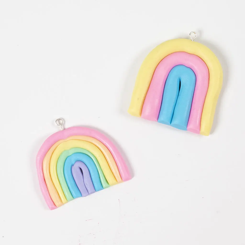 Twee afgewerkte regenboogjes van pastelkleurige klei met een ophangoogje.