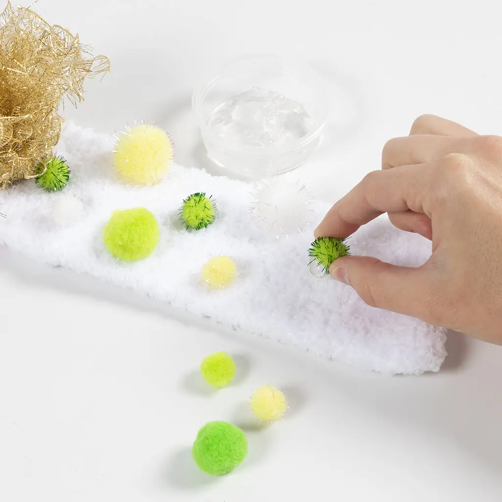 Verschillende gekleurde en glinsterende pompoms worden op de wreef van de pluizige witte sloef geplakt.