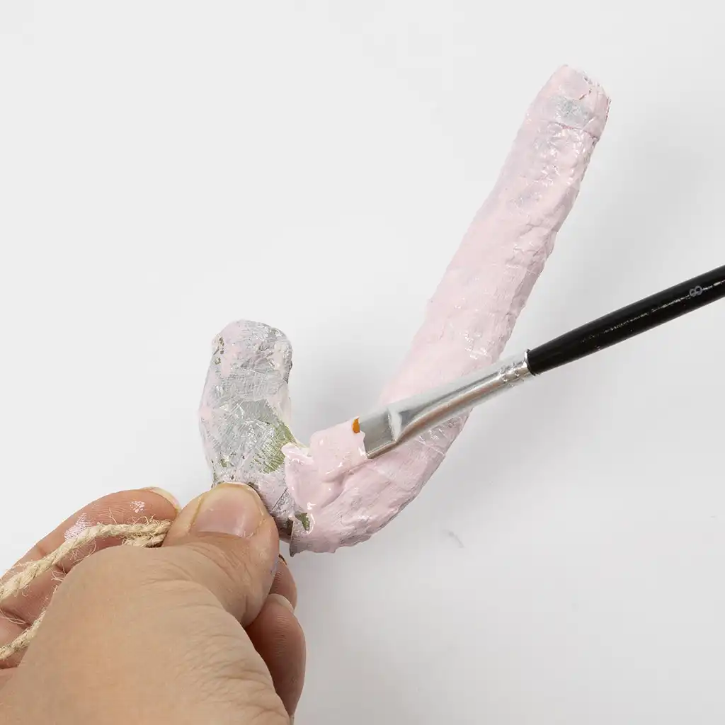 Een hand verft de zuurstok roze met een penseel.