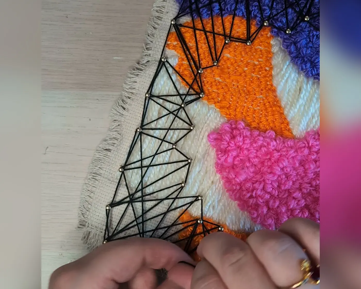 Close-up van handen die zwart garen spannen tussen spijkers op de hoek van het punch needle en string art werkstuk