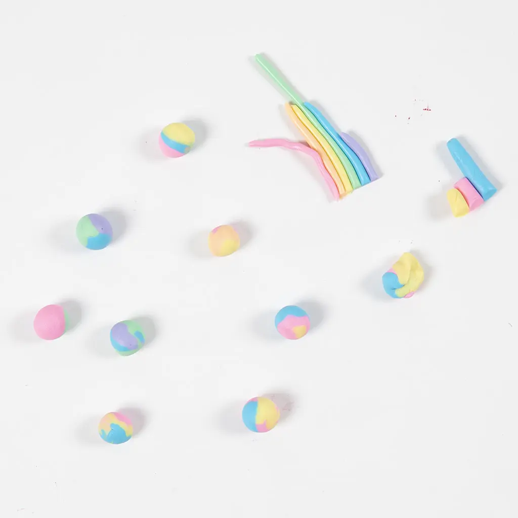 Restjes gekleurde klei en kleine gemarmerde kleibolletjes verspreid op een witte tafel.