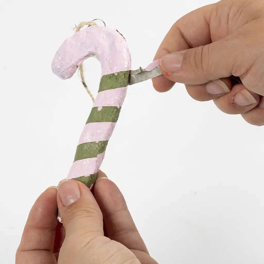 De stroken schilderstape worden voorzichtig van de zuurstok verwijderd, waardoor er een groen met roze gestreept patroon tevoorschijn komt.