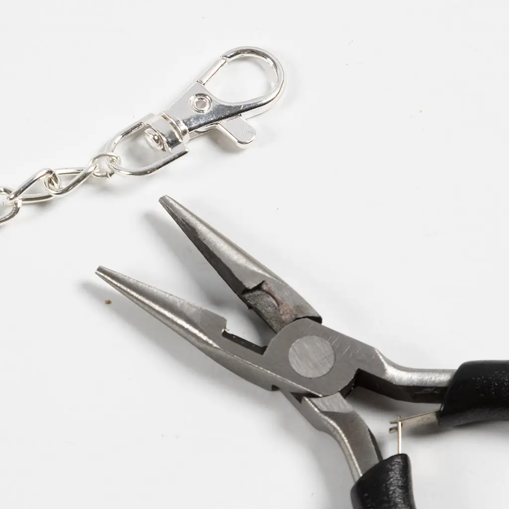 De zilveren karabijnsluiting is met behulp van het buigringetje en de tang stevig vastgemaakt aan het uiteinde van de schakelketting.