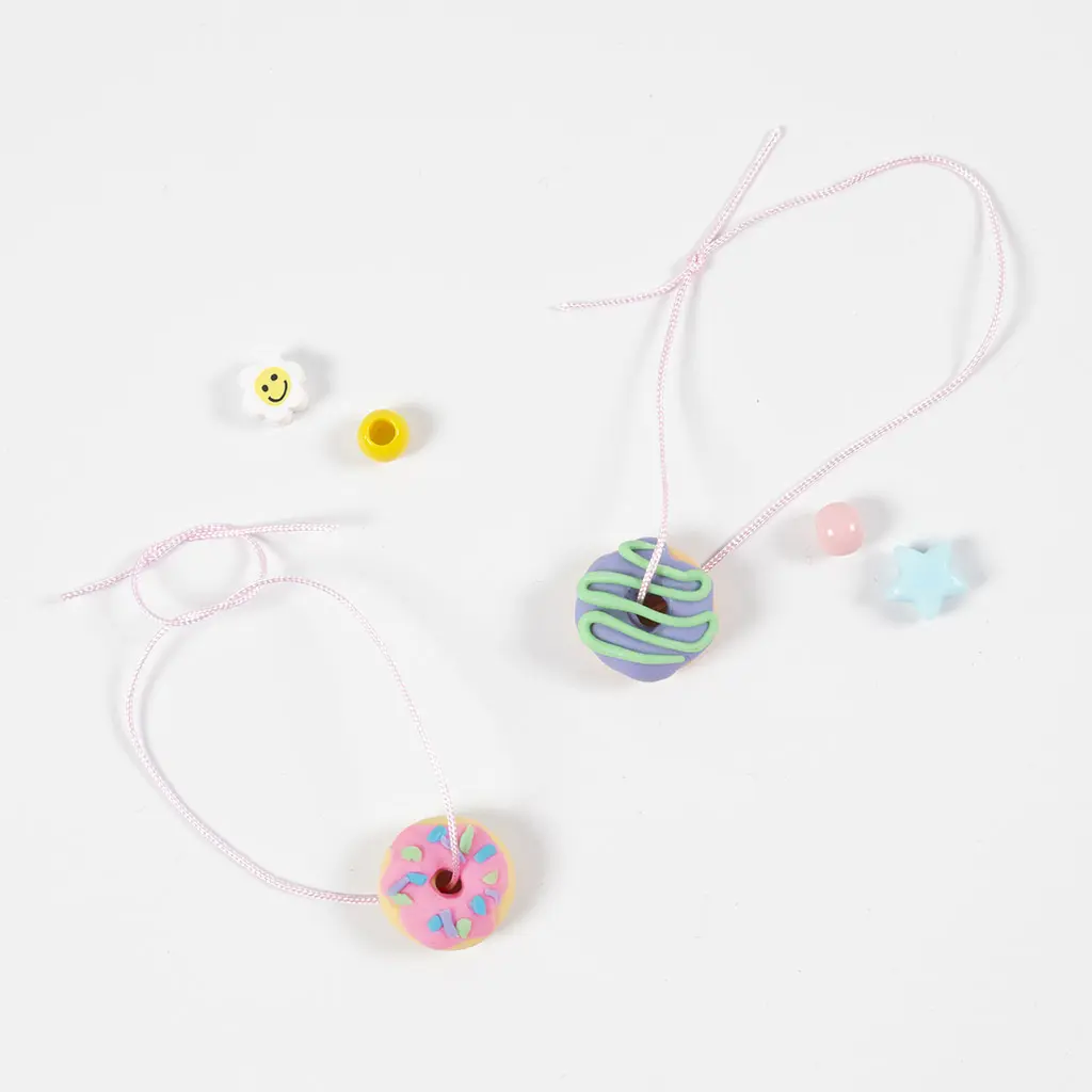 Roze draadjes gehaald door afgebakken kleidonuts om hangers of sieraden van te maken.