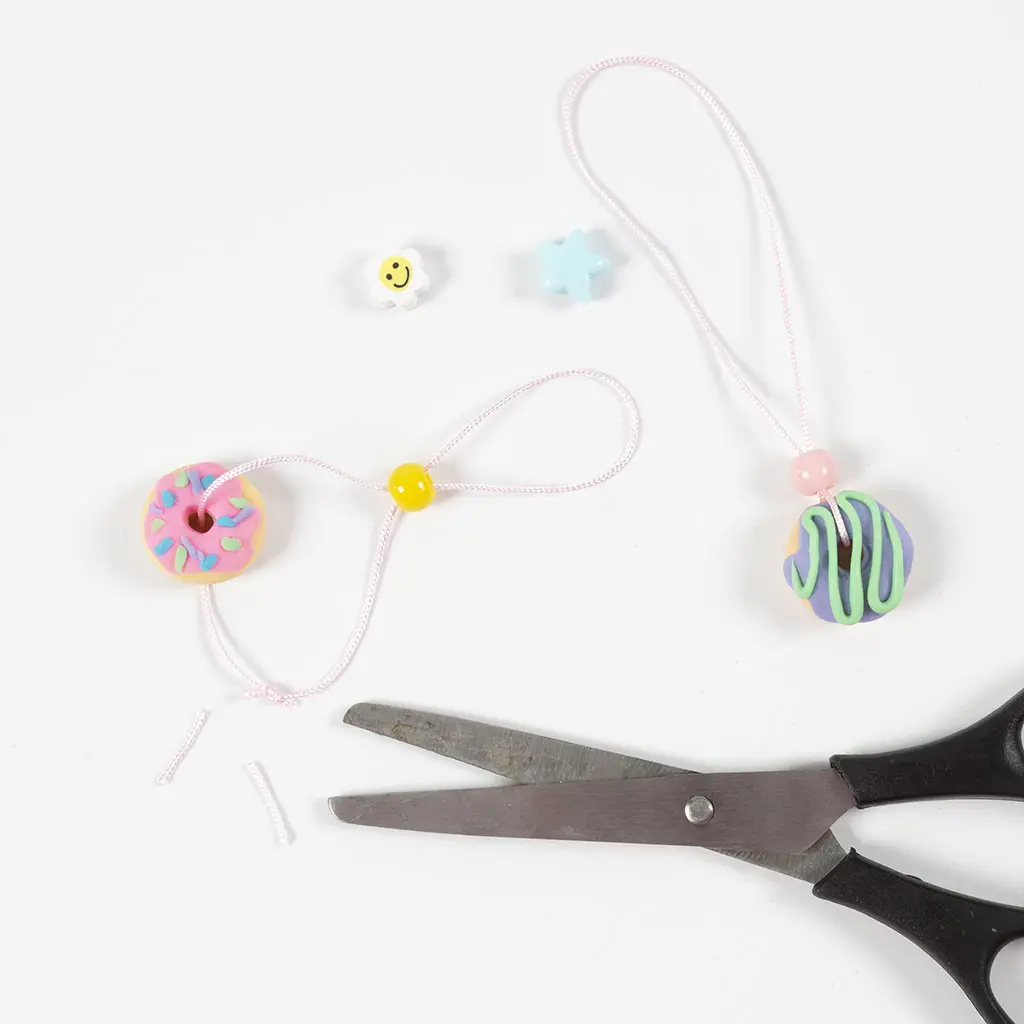 Afgewerkte sleutelhangers of kettingen van kleidonuts met extra kralen en een schaar op tafel.