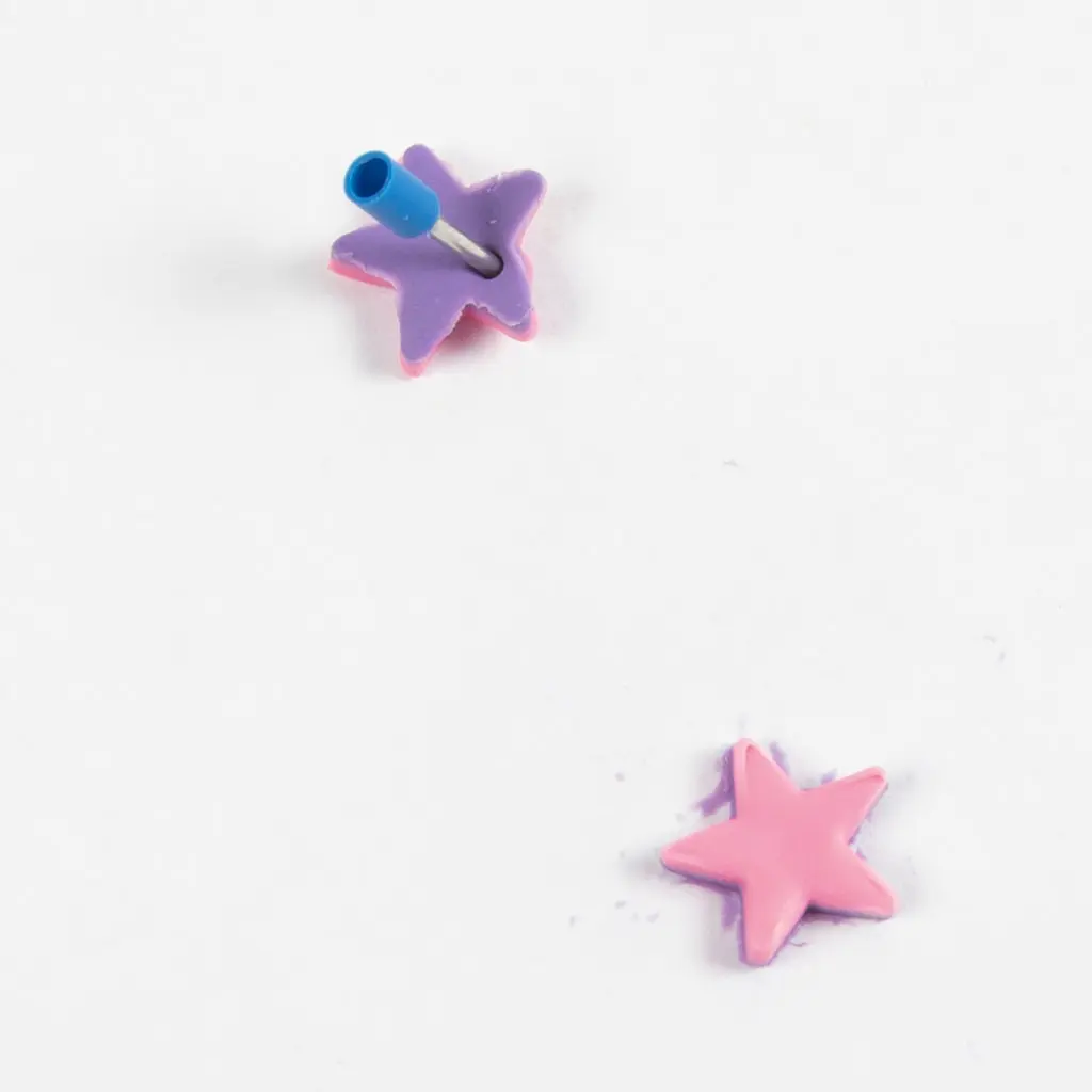 Een blauw hulpmiddel prikt een gaatje in de punt van een paars-roze kleisterretje, met een ander afgewerkt dubbellaags sterretje eronder.