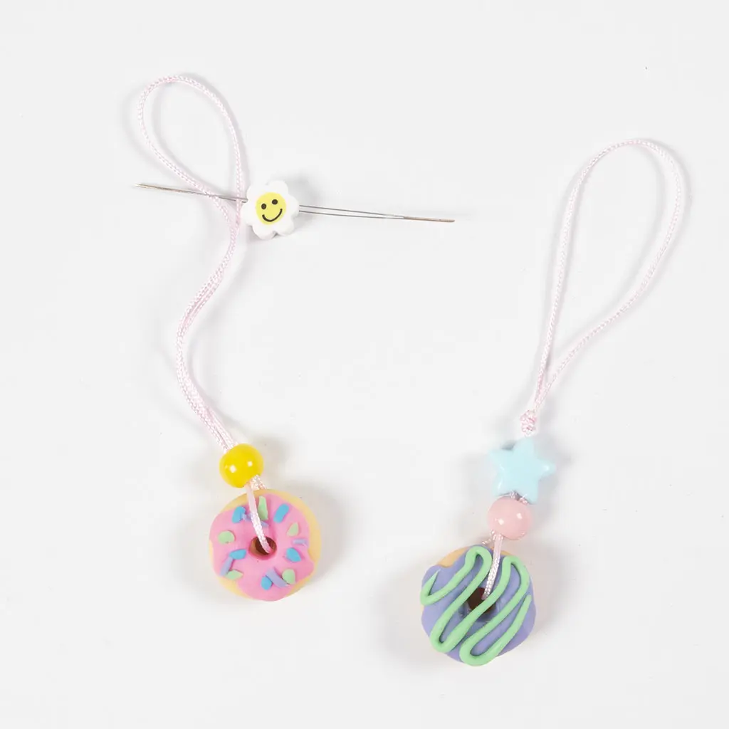 Rijgnaald en roze koord gebruikt om kralen en een kleidonut aan een lus te bevestigen.