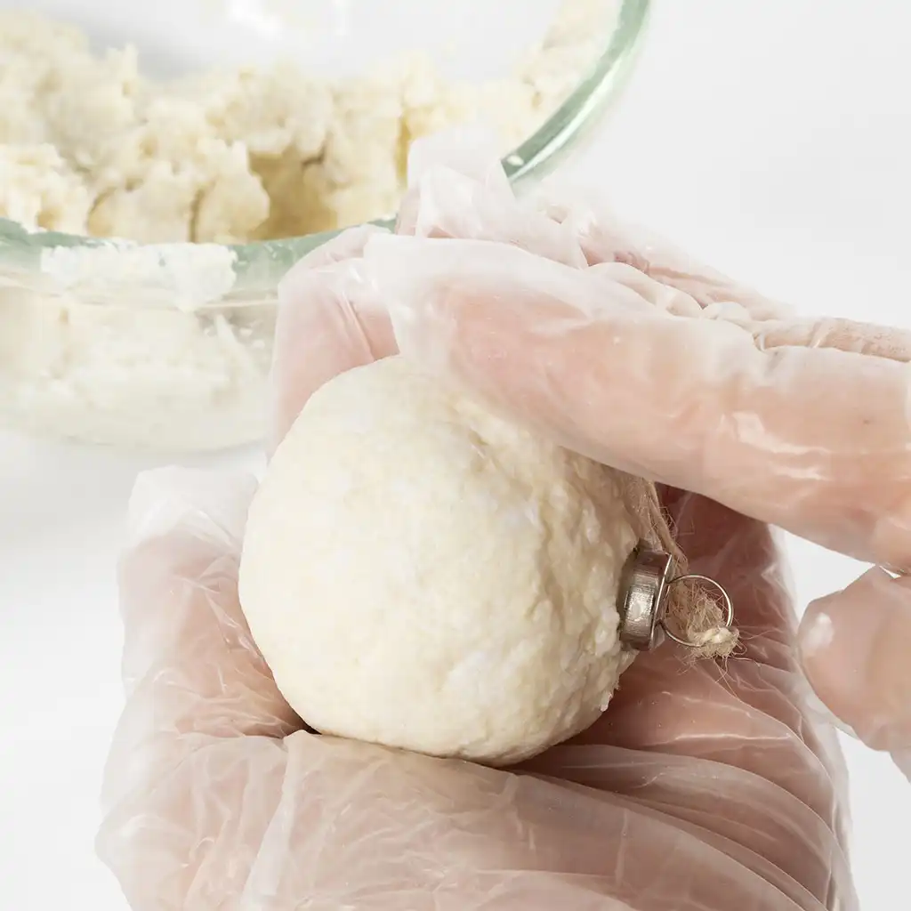 Twee handen met plastic handschoenen vormen en strijken de papierpulp glad rondom de piepschuim bol.
