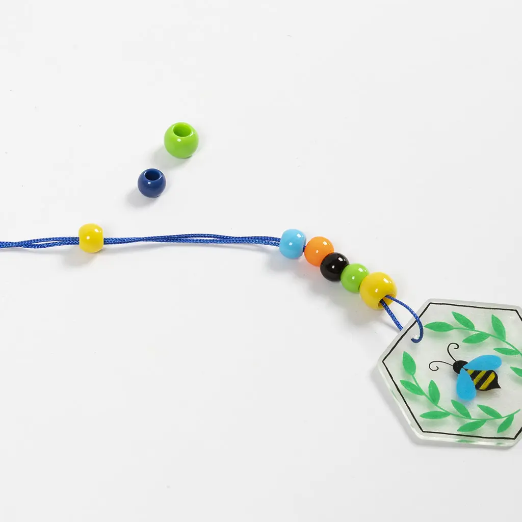Verschillende vrolijk gekleurde plastic kralen (geel, blauw, oranje, zwart, groen) worden aan het blauwe koord geregen vlak boven de bijen-hanger.