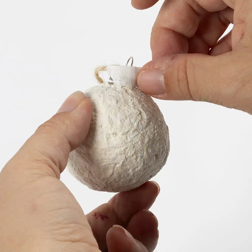 Een hand plakt een klein strookje schilderstape over het metalen kroontje van de bal van papiermaché om het af te dekken.