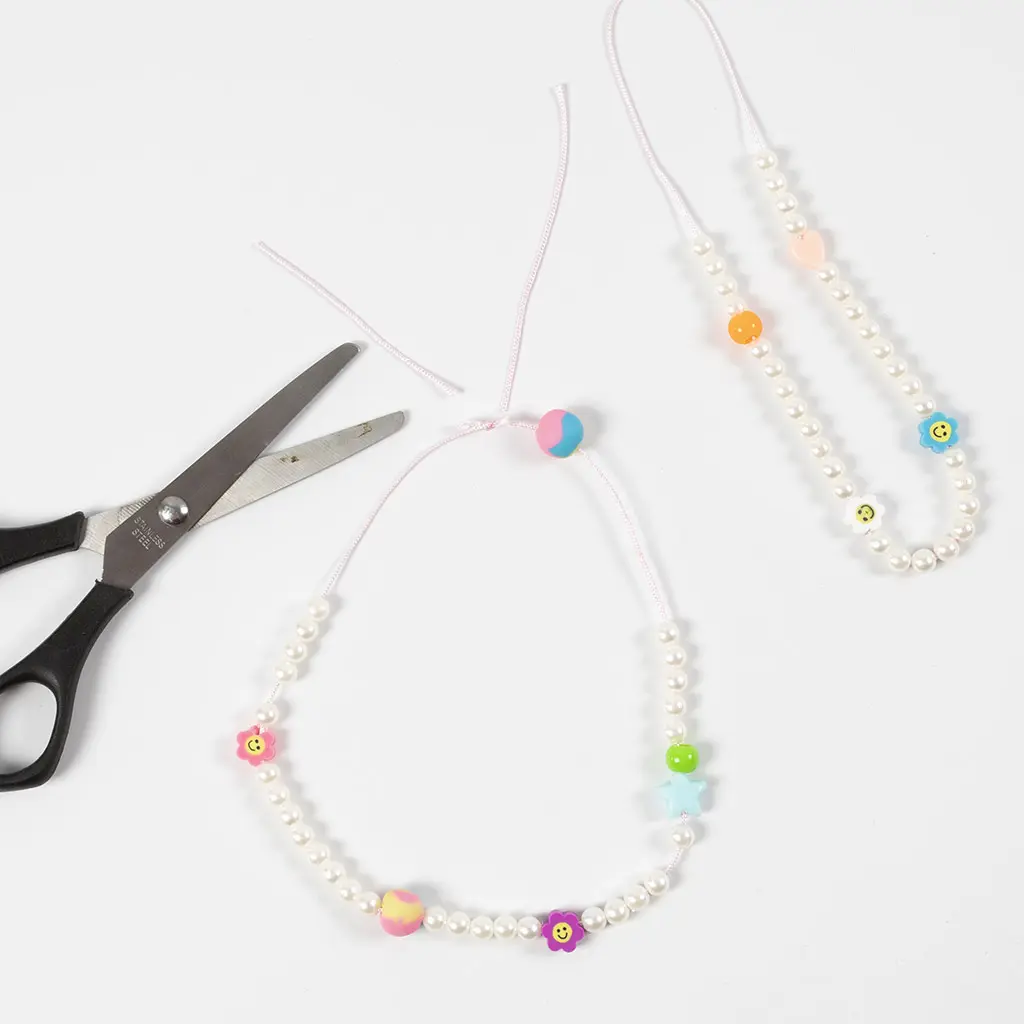 Het afknippen van de uiteinden van het roze koord bij de afgewerkte parelketting.