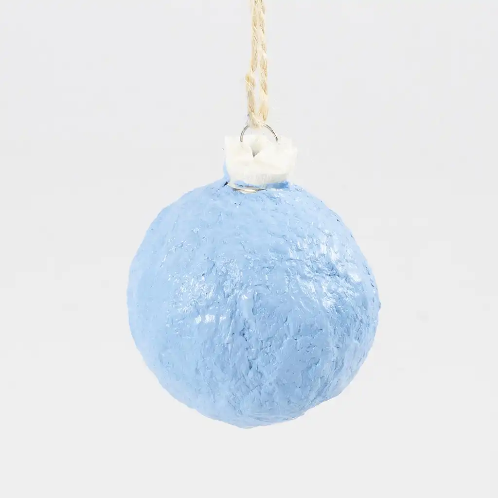 De lichtblauw geschilderde kerstbal van papiermaché hangt te drogen aan het jute touwtje.