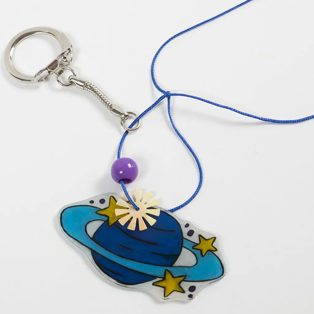 Een blauw koord wordt vastgeknoopt aan de ring van een metalen sleutelhanger met een klein kettingkje. Hieraan hangt een hanger van de planeet Saturnus, een paarse kraal en een goudkleurig zonnetje.