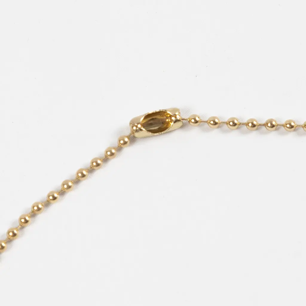Een close-up van een goudkleurige bolletjesketting die gesloten wordt met een bijbehorend metalen eind- of koppelstukje.