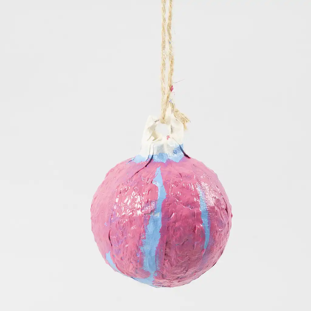 De volledig roze geschilderde kerstbal van papiermaché hangt te drogen aan het jute touwtje.