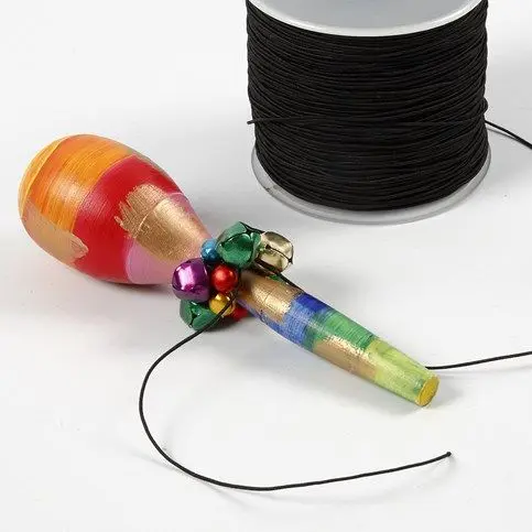 Het zwarte koord met de gekleurde belletjes is om de hals van een felbeschilderde houten maraca geknoopt, naast een rol zwart elastiek.