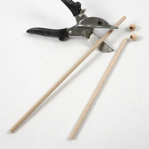 Een tang snijdt een houten stokje op maat voor het maken van drumstokjes, met twee losse houten kralen erbij.