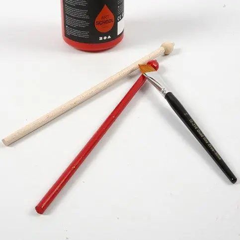 Eén van de houten drumstokjes met een kraal aan het uiteinde wordt met een penseel rood geverfd.
