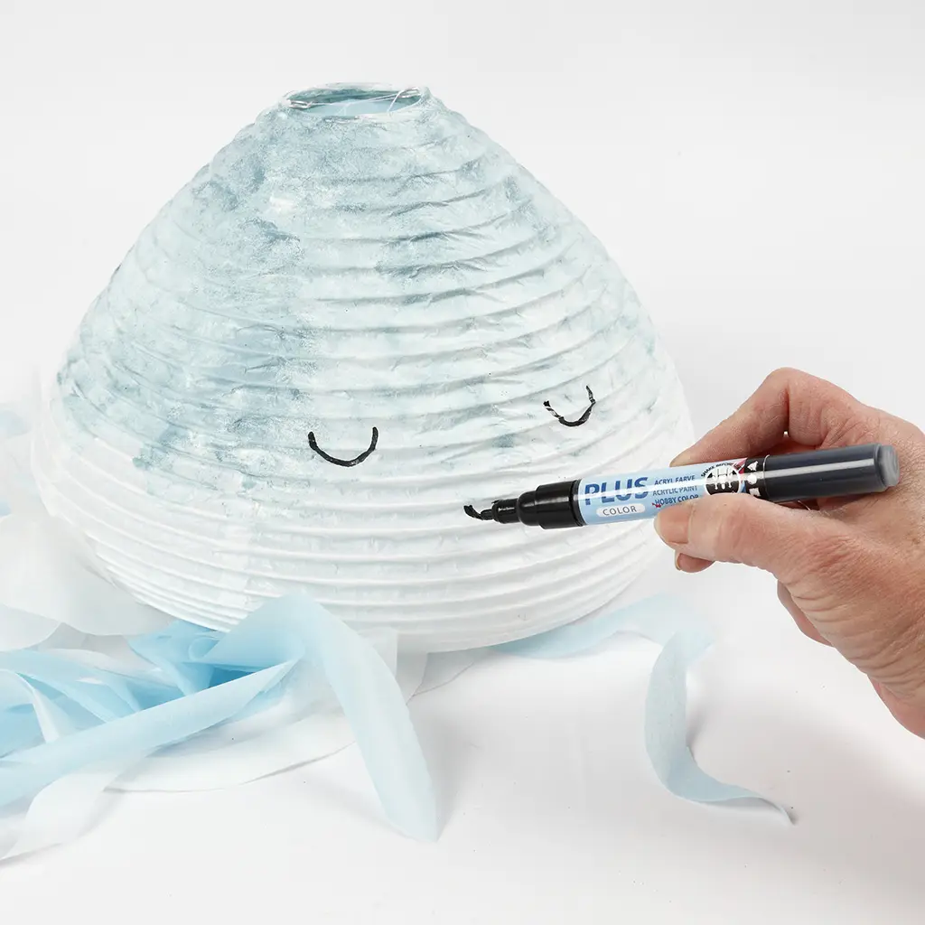 Met een zwarte acrylverfmarker worden twee blije oogjes getekend op de lichtblauw gesponste lampion.