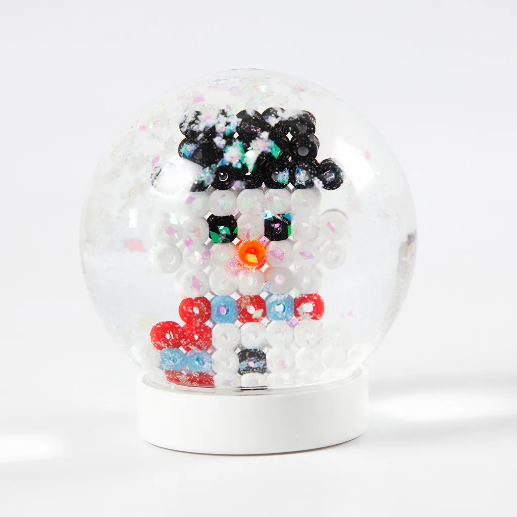 Een voltooide sneeuwbol op een witte voet met een sneeuwpop van strijkkraaltjes en dwarrelende glitters.