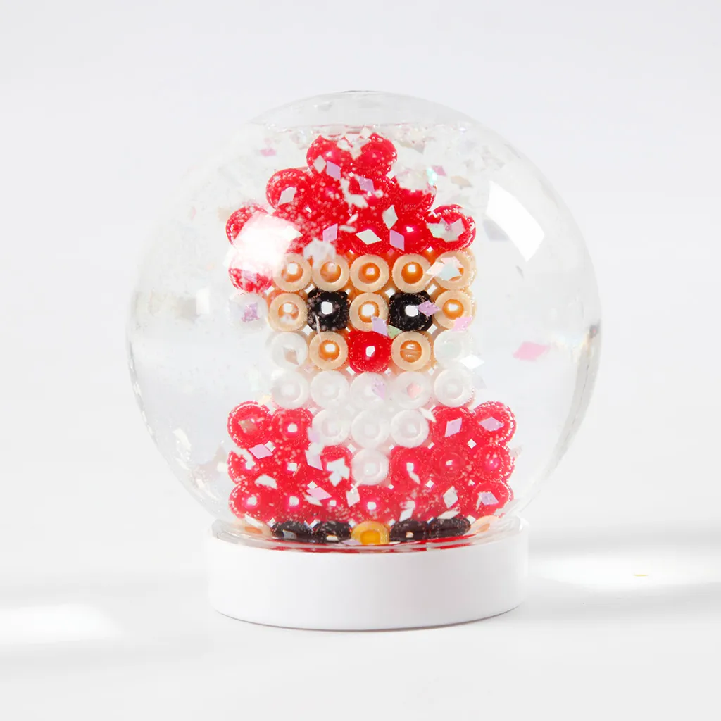 Een voltooide sneeuwbol op een witte voet waarin een kerstman van strijkkraaltjes staat omringd door glitters.