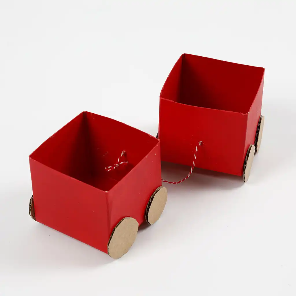 Twee rood geschilderde vierkante kartonnen wagons met kartonnen wieltjes zijn met elkaar verbonden door een rood-wit gestreept touwtje op een witte achtergrond.