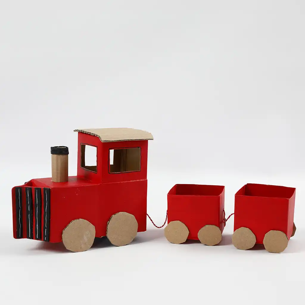 Het eindresultaat van een complete miniatuurtrein van karton, bestaande uit een rode stoomlocomotief met zwarte details en een schoorsteen, gevolgd door twee gekoppelde rode wagons op een witte achtergrond.