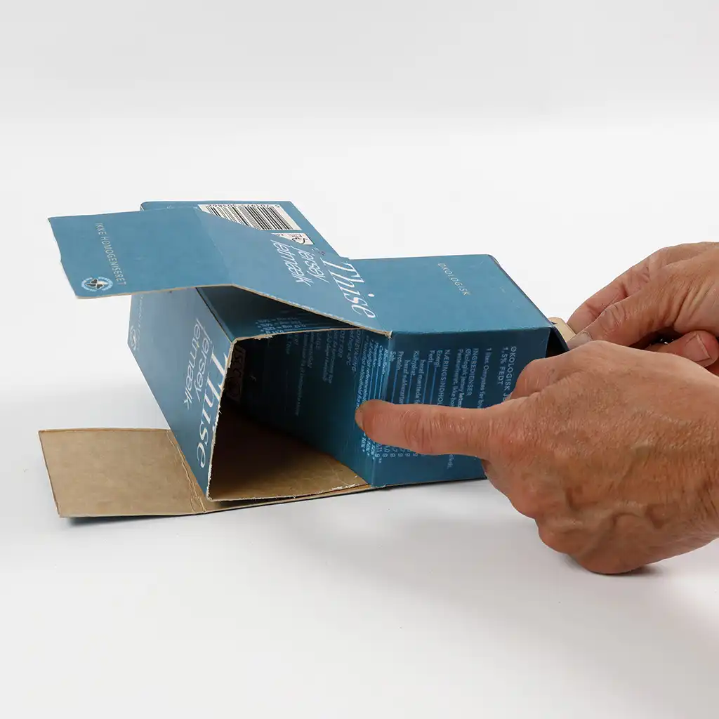Een hand schuift twee opengeknipte melkpakken in elkaar om de basis van de stoomlocomotief te vormen.