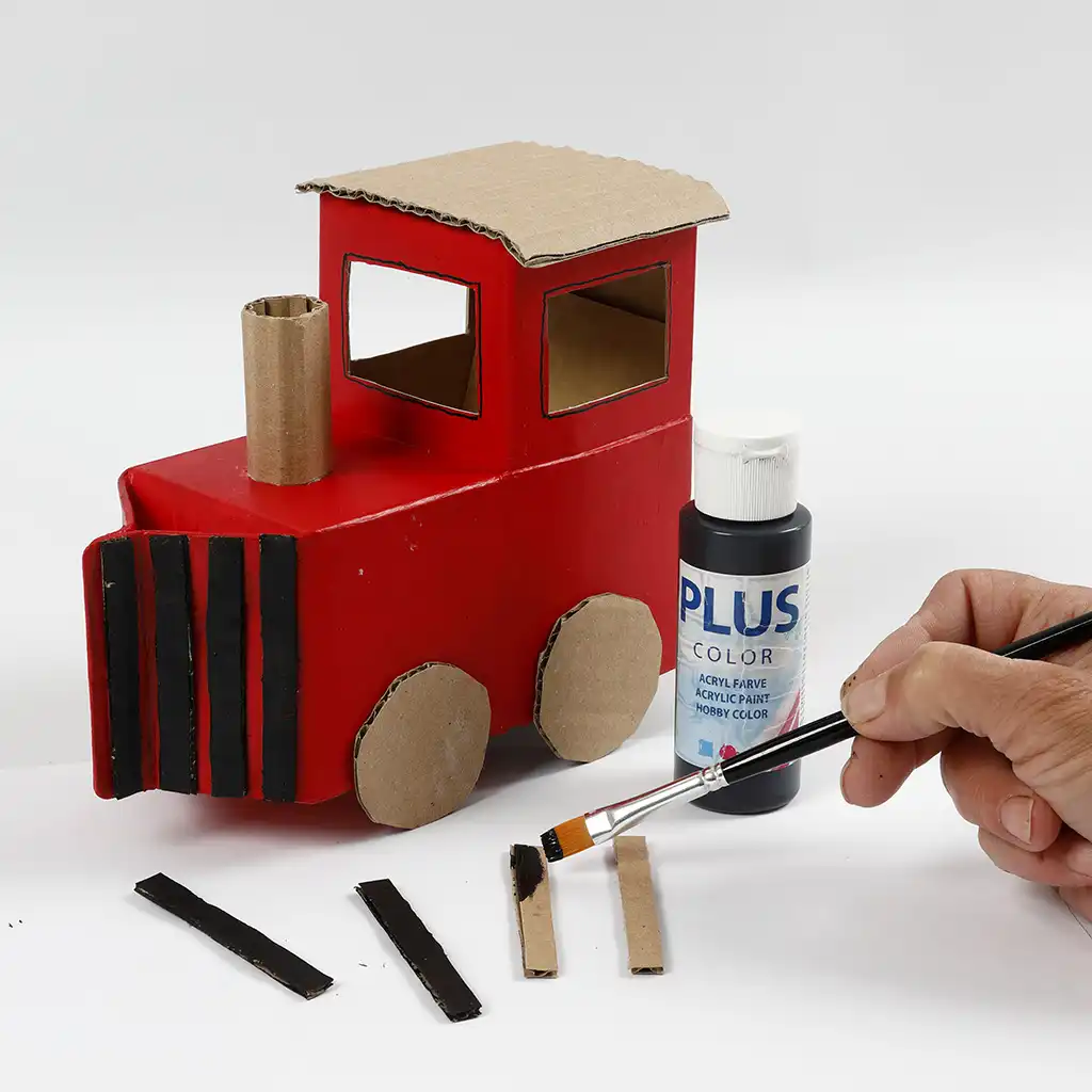 Een hand verft zwarte kartonnen stripjes met acrylverf voor de gril aan de voorkant van de stoomlocomotief.