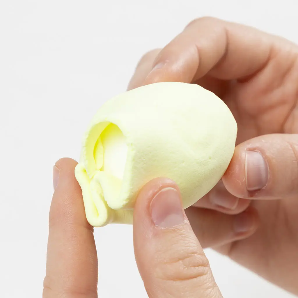 Het gladstrijken van de naden in de lichtgele klei aan de onderkant van het piepschuim ei.
