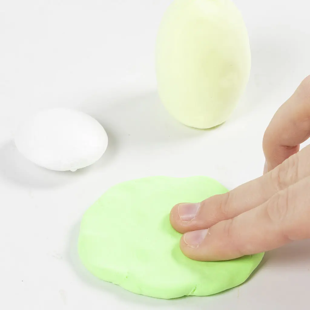 Het platduwen van felle groene klei tot een schijf, naast een ovaal schijfje van wit piepschuim.
