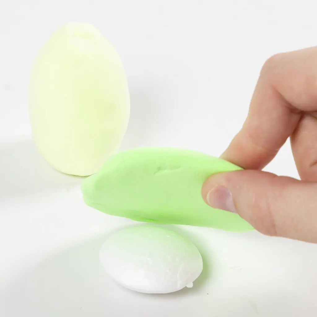 Het aanbrengen van de platte lap felle groene klei direct over het witte piepschuimen basisonderdeel.