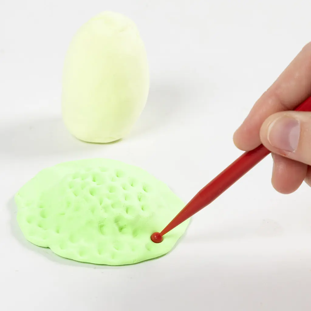 Het maken van kleine putjes in de groene kleibasis met een rode puntige dotting tool om een grastextuur toe te voegen.