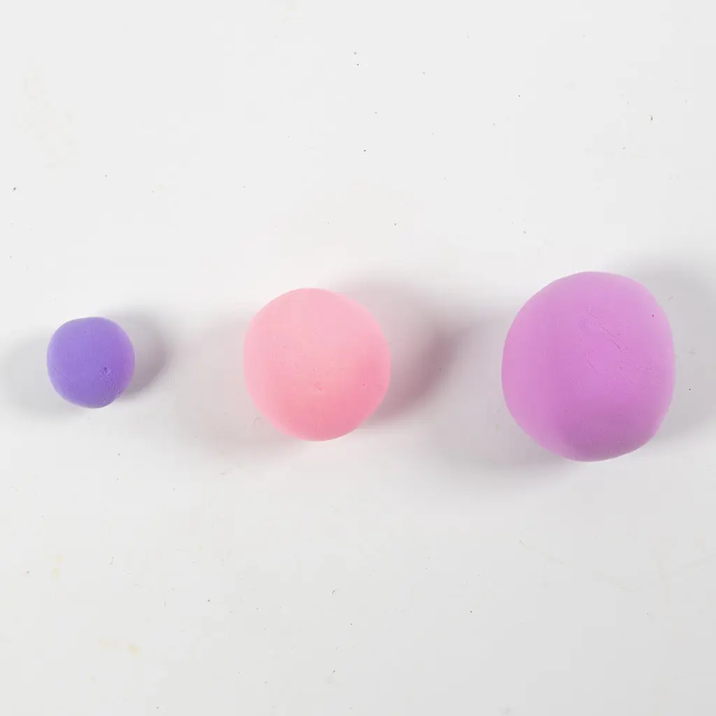 Drie op een rij gelegde kleibolletjes in paars, roze en paars/roze van oplopend formaat op een witte achtergrond.